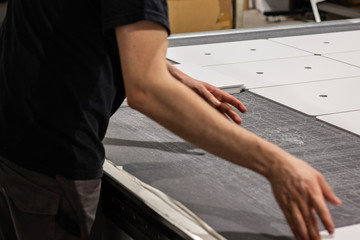 Worker, operating a cnc machine, delivering thin white boards cut into rectangular panels, ready for transport.