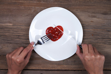 White dish with ketchup shaped as heart, hands with knife and fork.