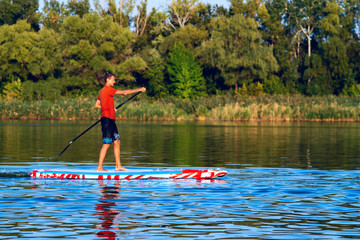 Fototapeta na wymiar Happy guy, teenager paddling on a SUP board on large river