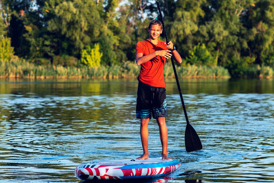 Happy guy, teenager paddling on a SUP board on large river