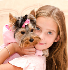 Adorable smiling little girl holding and playing with puppy yorkshire terrier