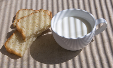 A glass of milk and pieces of white bread. The shadow of the blinds falls on the picture.