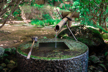 Obraz premium Ancient Zen stone wash basin with Japanese writings and water coming out of bamboo pipe in Ryoanji Temple, Kyoto, Japan