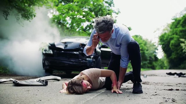 A man with telephone helping a young woman lying on the road after a car accident.