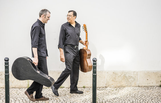 Two guitarists walking with their instruments on the street