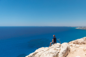 Fototapeta na wymiar Bald man in a T-shirt and shorts sitting alone on top of a mountain overlooking the sea