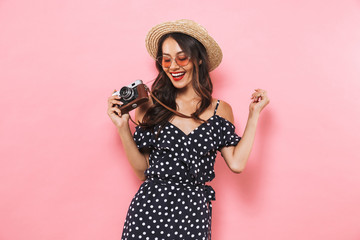 Naklejka premium Smiling brunette woman in straw hat and sunglasses making photo