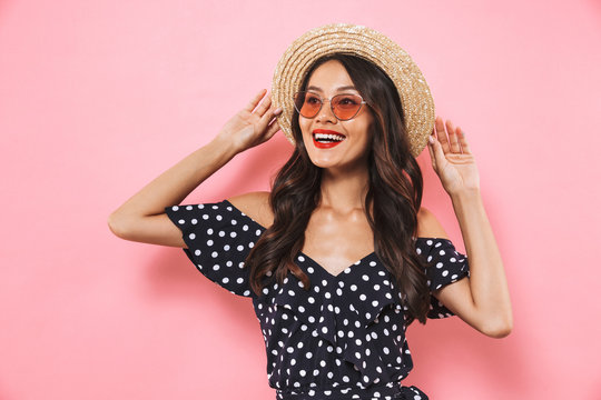 Pleased brunette woman in straw hat and sunglasses posing