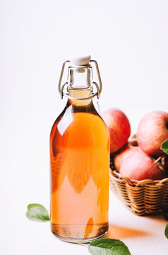 Apple vinegar in a bottle on white wooden table with apples in a basket.