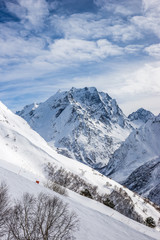 Fototapeta na wymiar Mt. Mussa-Achitara ski slope with Mt. Dombay-Ulgen on the horizon in winter sunny day. Dombai ski resort, Karachai-Cherkess, Western Caucasus, Russia.