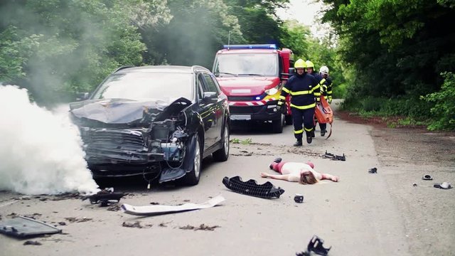 Firefighters rescuing a young injured woman lying on the road after an accident.