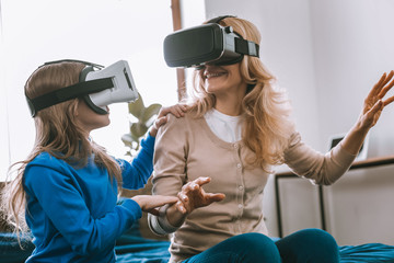New technology. Joyful nice mother and daughter smiling to each other while using virtual reality glasses