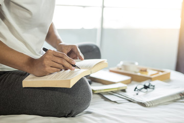 Young woman sitting working and writing in the notebook on bed leisure concept taking notes, Comfortable female workplace. Memories, planning , education.