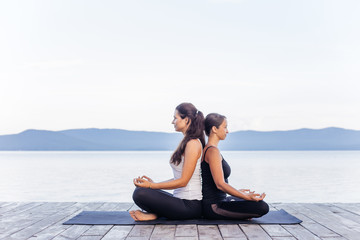 Fototapeta na wymiar Young attractive smiling women practicing yoga on a lake