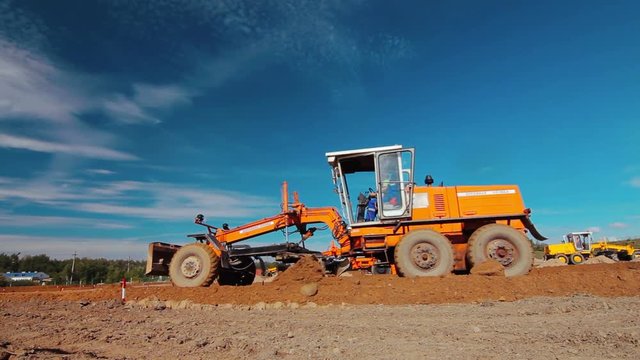 Orange wheel motor grader leveling ground on construction site. Heavy machinery in mining industry. Earth moving equipment working at quarry. Excavation building territory. Mining machinery