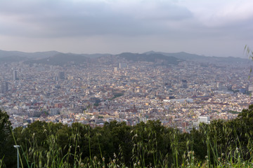 View to Barcelona city from the top of the Montjuic hill in cloudy day with bursts of sunlight. Barcelona skyline under grey clouds.