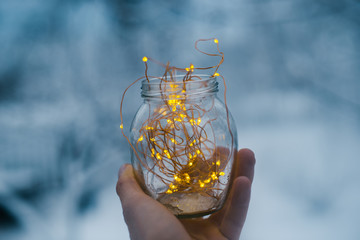 Fototapeta na wymiar Glass jar with garlands in hand in winter