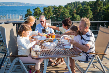 Big happy family having breakfast outdoors on terrace together, sitting around table, drinking...