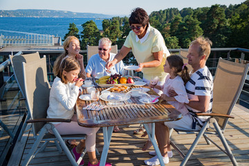 Big happy family having breakfast outdoors on terrace together, sitting around table, drinking coffee. Beautiful sea view, warm summer morning. Family bonds concept