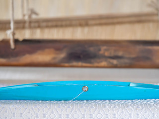 Fototapeta na wymiar Closeup of blue metal weaving shuttle and wooden loom.