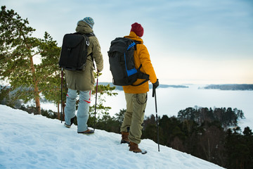 Two mature men with exploring Finland in winter. Travellers hiking and Taking pictures with camera on the top of rock. Beautiful view of northern landscape with frozen Baltic Sea and snowy islands.