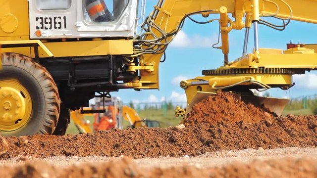 Motor grader leveling ground. Close up of construction machinery. Earth moving equipment working on construction site. Heavy earthmover technics working