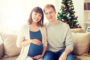 Obraz premium pregnancy, winter holidays and people concept - happy pregnant wife with husband at home at christmas
