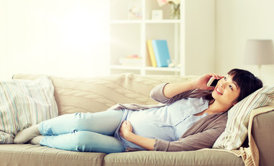 Obraz premium pregnancy, technology and people concept - happy pregnant asian woman calling on smartphone at home
