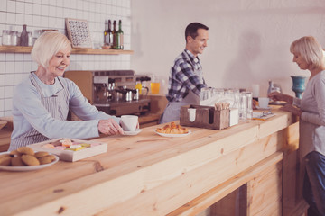 Work with pleasure. Pleasant cute senior woman standing in the kitchen near the bar smiling and...