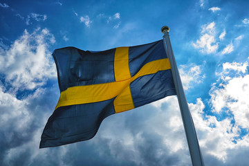 Flag of Sweden with blue sky and clouds at the background