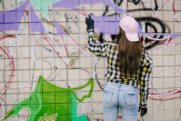 Young woman graffiti artist drawing on the wall, outdoor