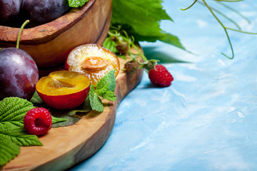 Closeup still life of plums and red raspberry with green leaves on wooden dish, summer autumn fall harvest