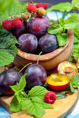 Closeup still life of plums and red raspberry with green leaves on wooden dish, summer autumn fall harvest