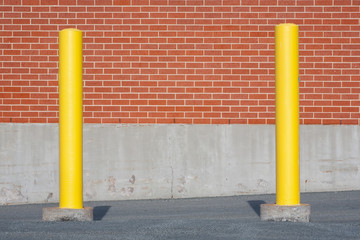 Yellow traffic bollards in front of brick building wall.