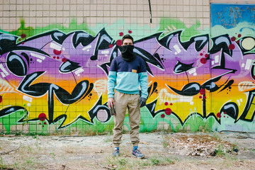 Young man graffiti artist in balaclava  with aerosol spray bottle near the wall