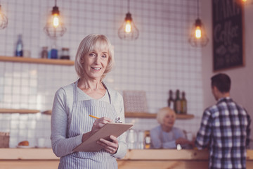 Confident senior responsible woman standing in the bright room holding a tablet and smiling.