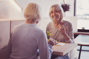 Best company. Satisfied aged friendly woman sitting by the table smiling and talking to her girlfriend.