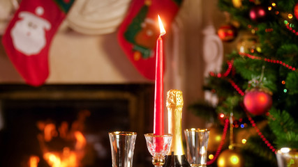 CLoseup image of burning festive candle against fireplace and decorated Christmas tree