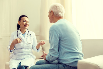 Fototapeta premium Regular checkup. Selective focus on a smiling lady gesturing while talking to a retired gentleman during a medical consultation.