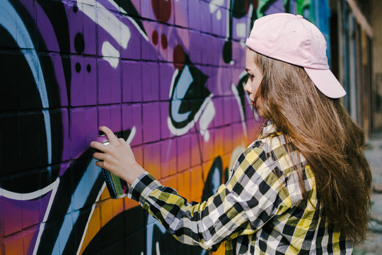 Young woman graffiti artist drawing on the wall, outdoor