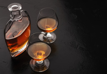 Two glasses of brandy or cognac and bottle on black - obrazy, fototapety, plakaty