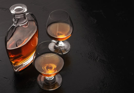 Two glasses of brandy or cognac and bottle on black