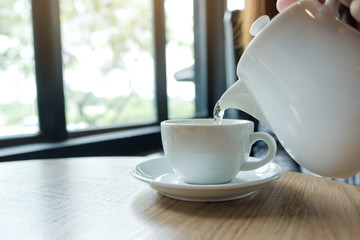 A hand holding teapot and pouring tea into a white cup on wooden table