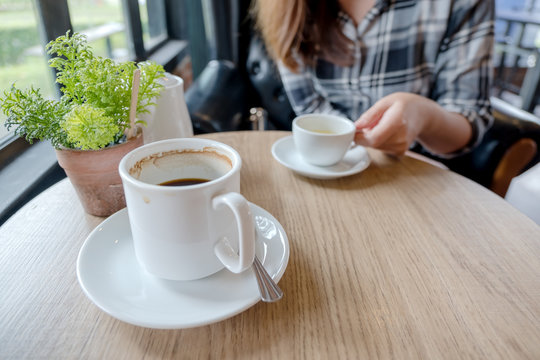 Closeup image of a woman holding a white cup of hot tea with a mug of coffee on wooden table in cafe