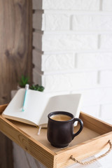 A cup of coffee and an open notebook on a wooden tray in the light interior of the apartment. Cozy home