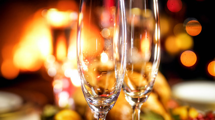 Closeup image of empty champagne glasses against burning fireplace and glowing Christmas tree