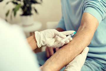 Medicine is the best medication. Scaled up look on a female medical professional wearing gloves holding an arm of a retired patient while vaccinating him.