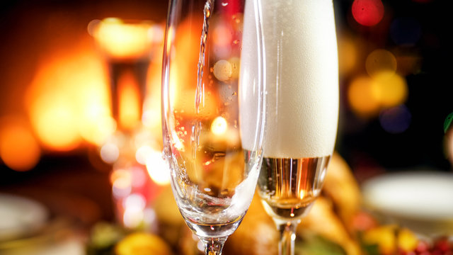 Closeup image of champagne flowing in two glasses against burning fireplace