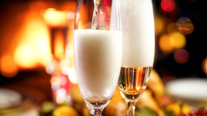 Closeup image of pouring champagne in glasses on romantic Christmas dinner