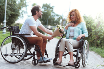 Unexpected gift. Mindful gentleman giving amazed lady a bouquet of flowers while they going on a date outdoors.